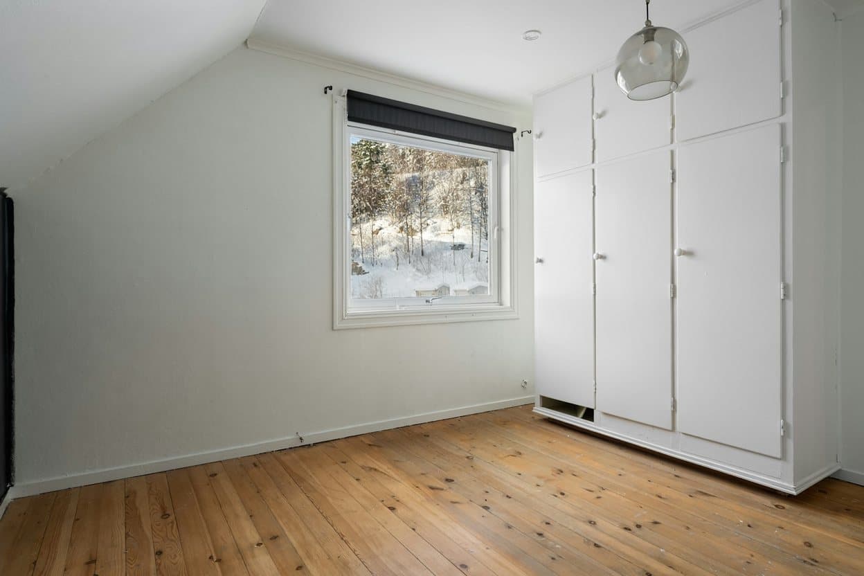 A small attic bedroom with a sloped ceiling, a window and built-in wardrobes